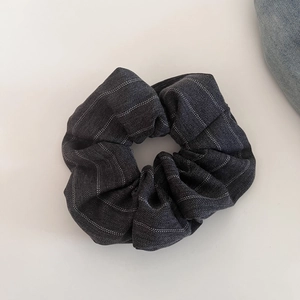 Detail of dark grey herringbone fabric scrunchie with white vertical stripes on ivory surface