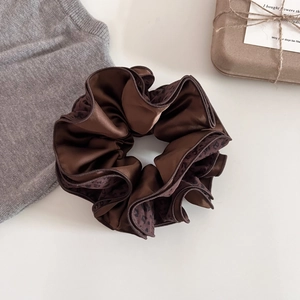Close-up of brown satin leopard print scrunchie on minimalist aesthetic background