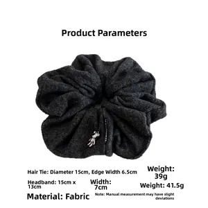 Close-up of large grey scrunchie with silver bear charm and branded woven label