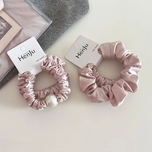 Detail of pink satin hair scrunchies set featuring a large pearl and smooth silk texture