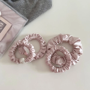 Detail of four pink satin scrunchies featuring soft pleats and elegant pearl embellishment