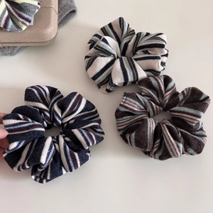 Detailed texture of three knitted striped scrunchies in cream, blue, and brown colors