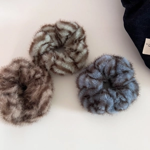 Close-up of three plush faux fur zebra pattern scrunchies in brown and blue colors
