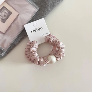 Detailed macro view of a soft pink satin scrunchie featuring an elegant faux pearl accent