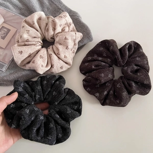 Detailed view of three floral knit scrunchies in beige, dark brown and black colors