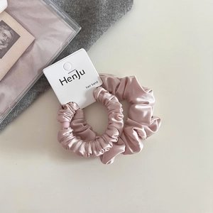 Detail of pink satin scrunchie with soft pleats and a branded paper hang tag