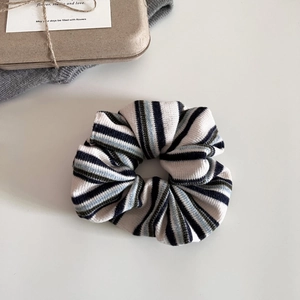 Detailed texture of a striped knit scrunchie styled with aesthetic art cards and packaging