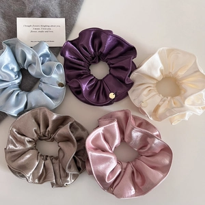 Détail de cinq chouchous en satin nacré avec breloques dorées aux couleurs élégantes