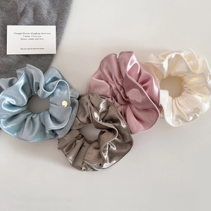 Détail de quatre chouchous en satin bleu, doré, rose et blanc avec badges métal