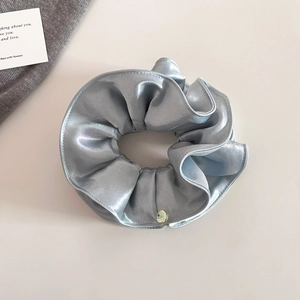 Détail d'un chouchou en satin gris argenté avec plis superposés et breloque en métal doré