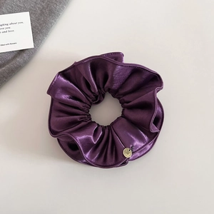 Détail du chouchou en satin plissé violet foncé avec un petit charme en métal doré