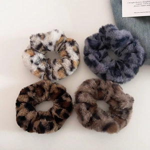 Close-up of four plush leopard print scrunchies in various colors for winter hair styles