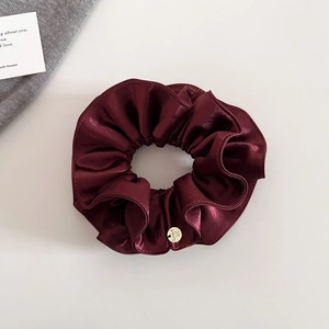 Détail du chouchou en satin bordeaux avec plis superposés et médaillon rond en métal doré