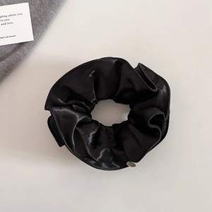 Gros plan du chouchou en satin noir avec étiquette métallique sur fond minimaliste