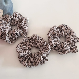 Close-up of three leopard print scrunchies with knitted texture and brand labels