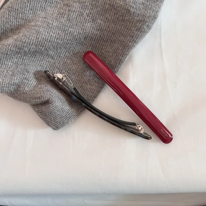Minimalist burgundy and black acetate hair clips on a soft grey knitted background