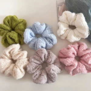 Set of six fluffy knitted scrunchies in pastel colors on a soft neutral background