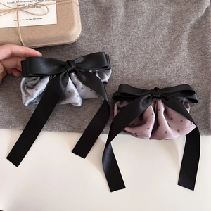Close-up of two elegant polka dot satin bow hair clips with long flowing ribbons in soft grey