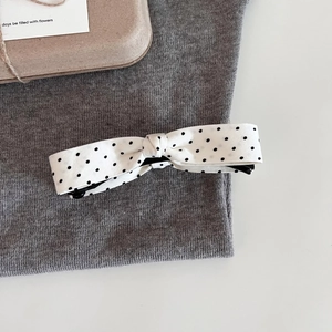 Close-up of white fabric bow hair clip with black polka dots on a soft grey textile