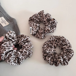 Three-piece set of leopard print fabric scrunchies on grey knit sweater background