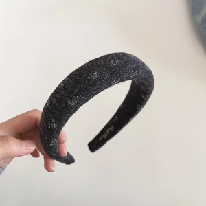 Detailed macro view of black sponge headband with thick tweed texture and gold logo