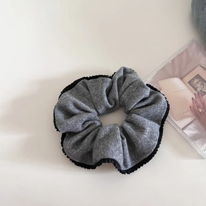 Close-up of grey knitted scrunchie with black ruffled edges on minimalist aesthetic background