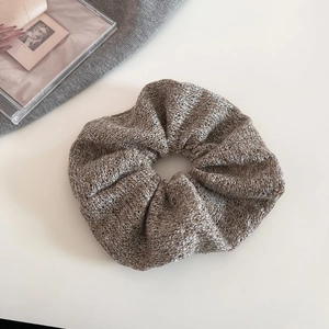 Close-up of a soft grey knitted scrunchie with textured fabric on a white background