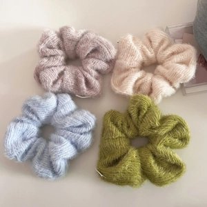 Detail of four knitted scrunchies in pastel colors with soft plush texture and elastic bands