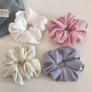Detail of four waffle knit hair scrunchies in pastel pink, white, beige, and light purple