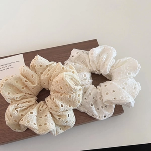 Close-up of two hollow lace scrunchies in white and beige on a wooden stand