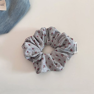 Gros plan sur un chouchou floral gris avec texture côtelée et étiquette de marque