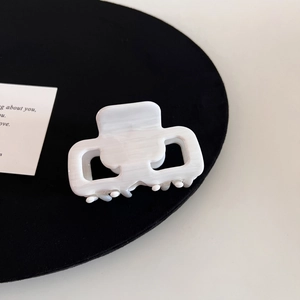 Detail shot of a square acetate hair claw with elegant cream marble texture and secure grip