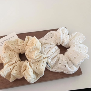 Detail of white and beige hollow lace scrunchies with floral embroidery on wooden base