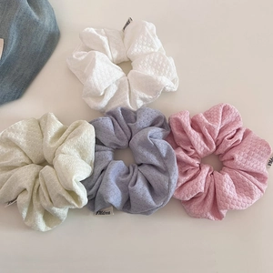 Detailed view of four colorful waffle texture knit scrunchies with brand labels