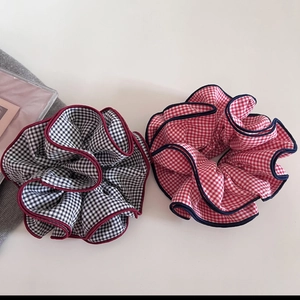 Detailed view of two checkered scrunchies with red and navy contrast edges on gray fabric