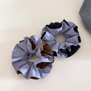 Detail of two-tone pleated hair scrunchies showing fabric texture and woven brand label