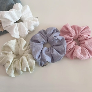 Close-up of four soft knit bubble hair scrunchies in pastel pink purple white and beige