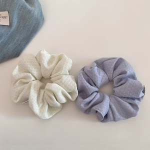 Close-up of large cream and lilac textured bubble knit scrunchies with brand tag detail