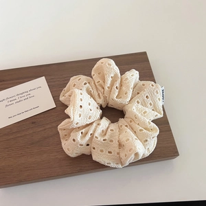 Detailed view of beige hollow-out lace scrunchie on dark wooden tray with prop card