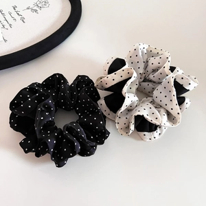 Close-up of two elegant polka dot satin scrunchies in black and white on a white surface