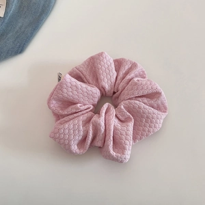 Close-up of pink waffle knit scrunchie featuring a white decorative woven FINE tag