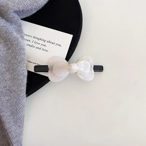 Detailed view of pearlescent white acetate bow hair clip on elegant black stand