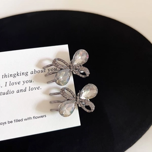 Detailed macro view of two gunmetal rhinestone bow hair clips on a white display card