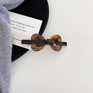 Detailed close-up of tortoise shell pattern acetate bow hair clip on a soft gray background
