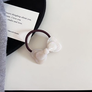 Close-up of a pearly white resin bow hair tie with a durable dark brown elastic band