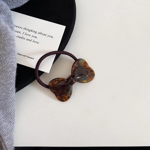Detail of tortoiseshell pattern hair tie with resin bow ornament on a textured background