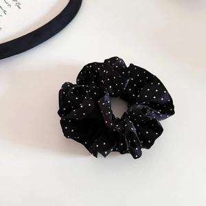 Close-up of black satin scrunchie with white polka dots and soft pleated silk texture