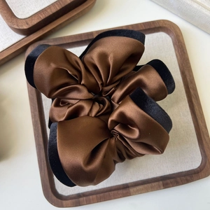Close-up of brown satin scrunchie with black velvet edges on a wooden tray