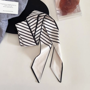 Gros plan d'un foulard élégant en soie à rayures noires et blanches sur tissu gris