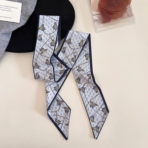 Flat lay detail of a light blue skinny silk scarf with butterfly and chain prints